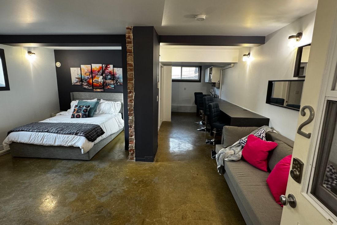 La Grange studio suite seen from the entrance, with a queen bed, colourful wall art, grey sofa and counter seating